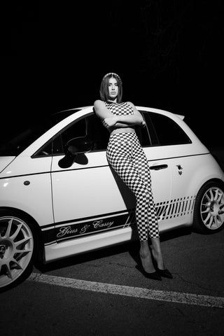 Set activewear donna Elise Daytona a scacchi bianco nero con posa in piedi appoggiata all’auto bianca