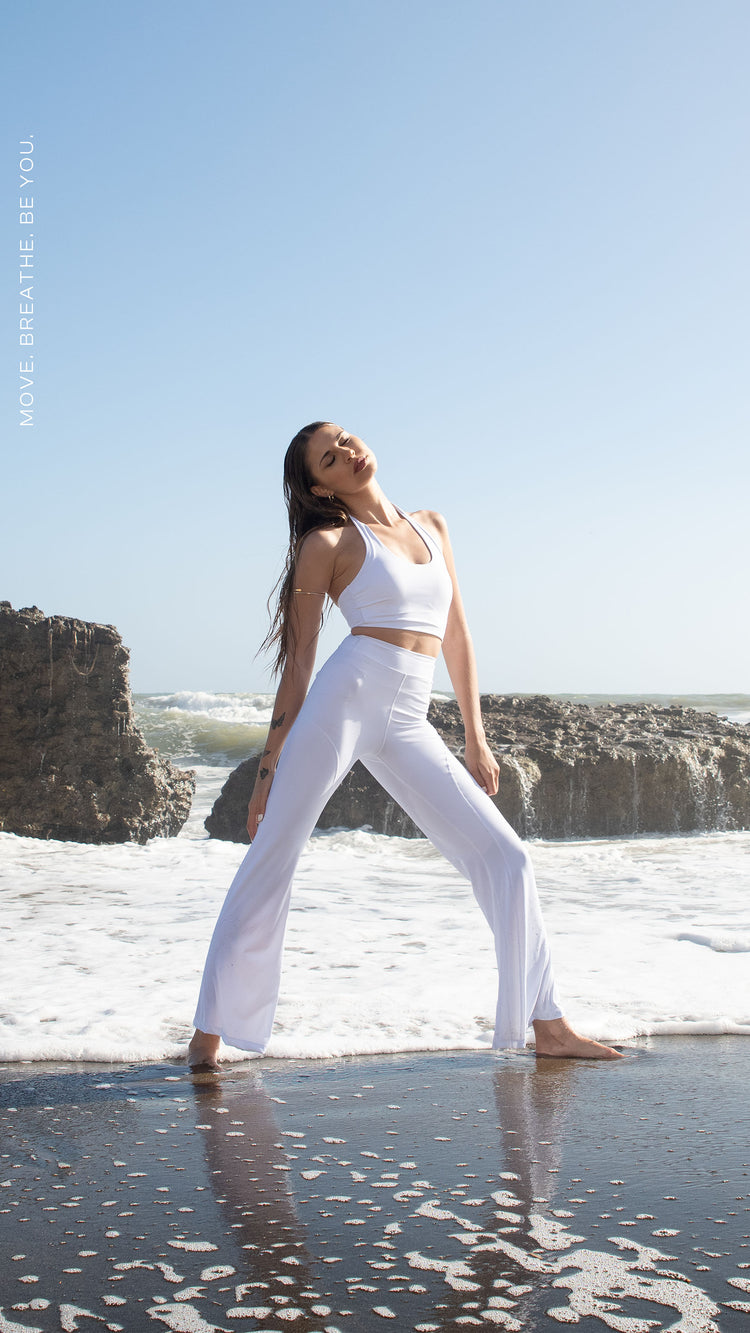 Set activewear donna Sincera bianco con leggings a zampa in posa ampia sulla battigia davanti alle onde del mare