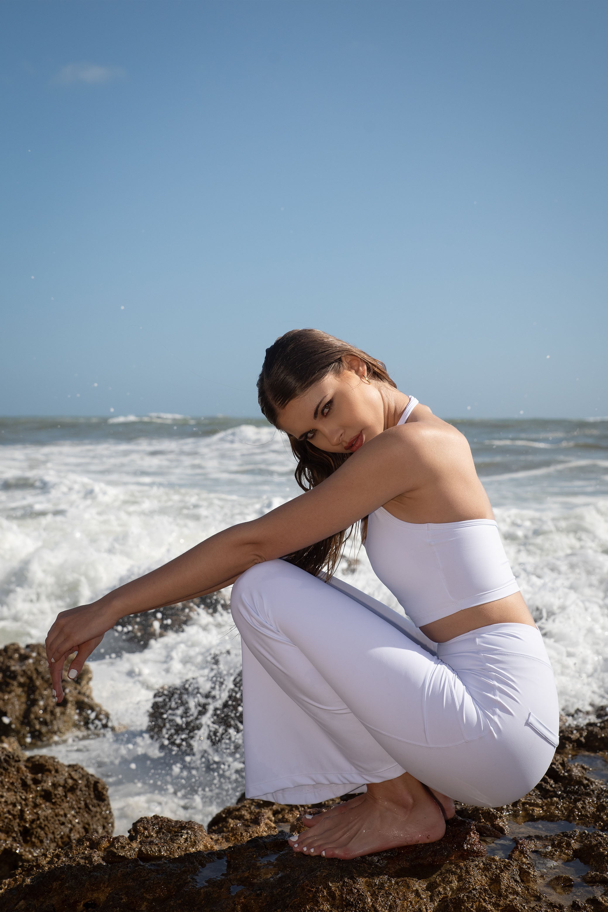 Set activewear donna Sincera bianco con leggings a zampa accovacciata sugli scogli davanti al mare