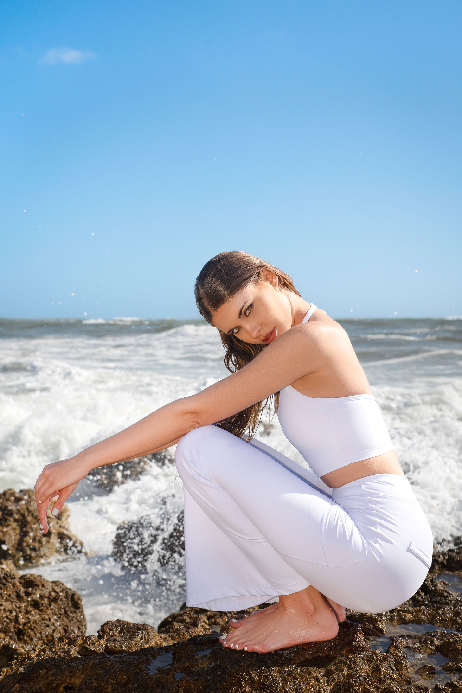 Set activewear donna Sincera bianco con leggings a zampa accovacciata sugli scogli davanti al mare