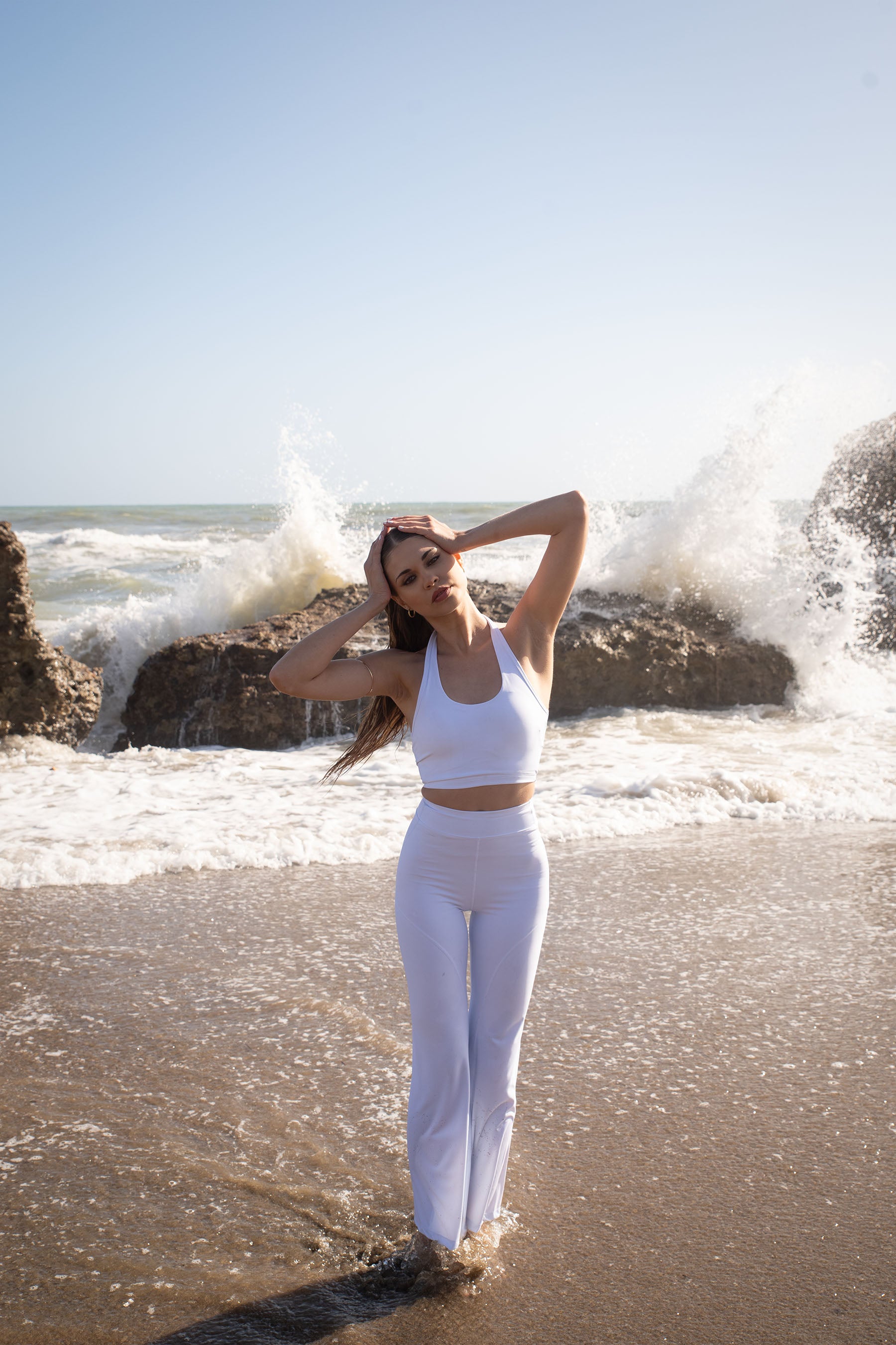 Set activewear donna Sincera bianco con leggings a zampa sulla battigia davanti alle onde del mare
