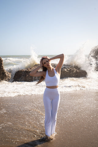 Set activewear donna Sincera bianco con leggings a zampa sulla battigia davanti alle onde del mare
